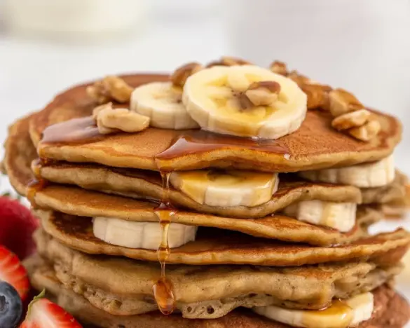 Fluffy Keto Banana Nut Protein Pancakes topped with nuts and syrup on a plate.
