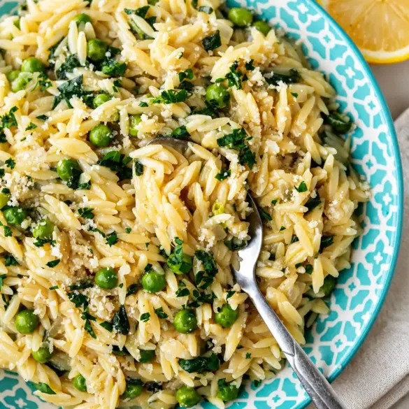 Bowl of Greek Lemon Orzo with Spinach garnished with lemon slices and herbs.